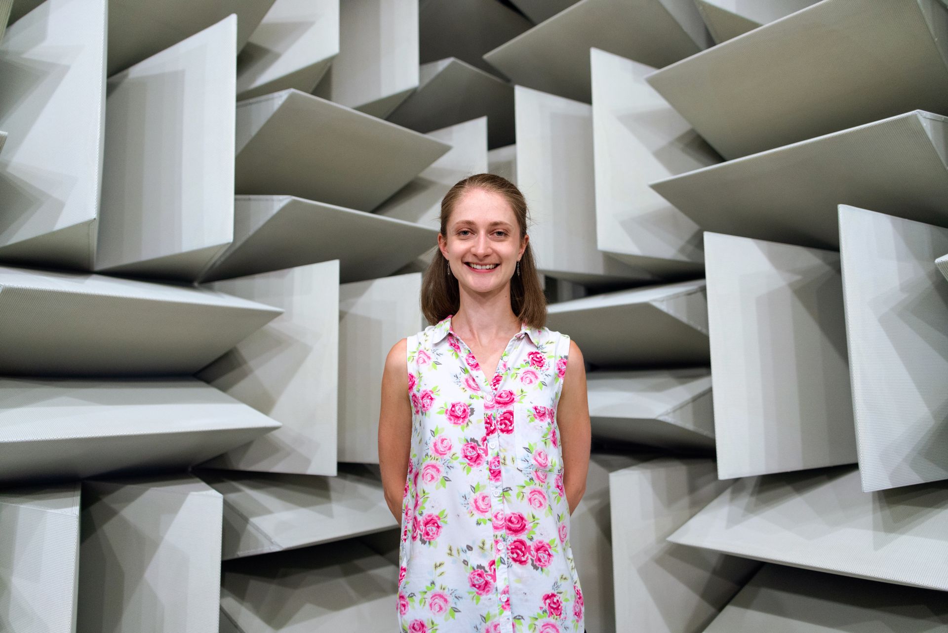 Smiling woman standing inside an acoustic engineering chamber with soundproof panels.