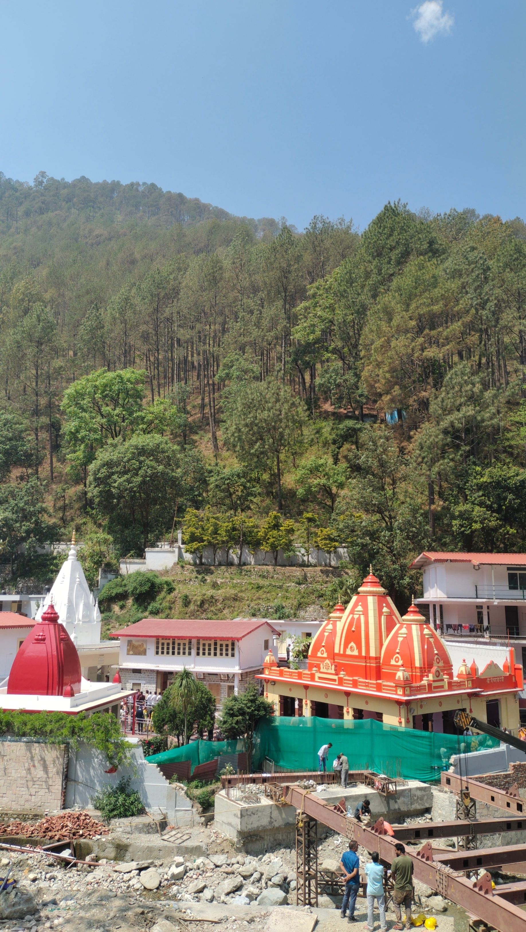 Beautiful Hindu temples located in a scenic hillside with lush green trees under a clear blue sky.