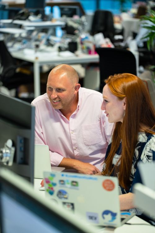 Free Two colleagues collaborating at a desk in a modern office environment, smiling and engaged. Stock Photo