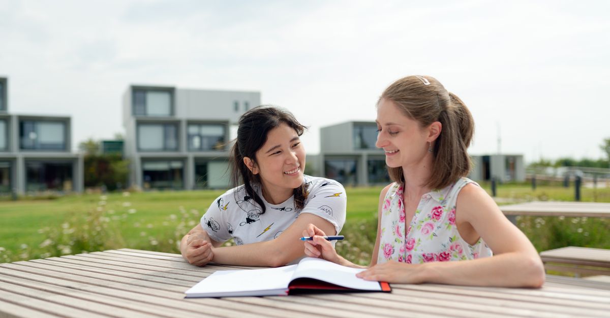 A student and principal sitting together on a bench, having a genuine conversation with smiles