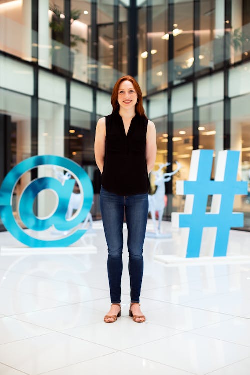 Free Woman In Black Sleeveless Shirt And Blue Denim Jeans Standing On White Floor Tiles Stock Photo