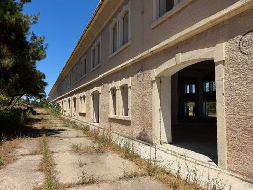 Free Sunlit exterior of a long-abandoned building with open windows and overgrown pathway. Stock Photo