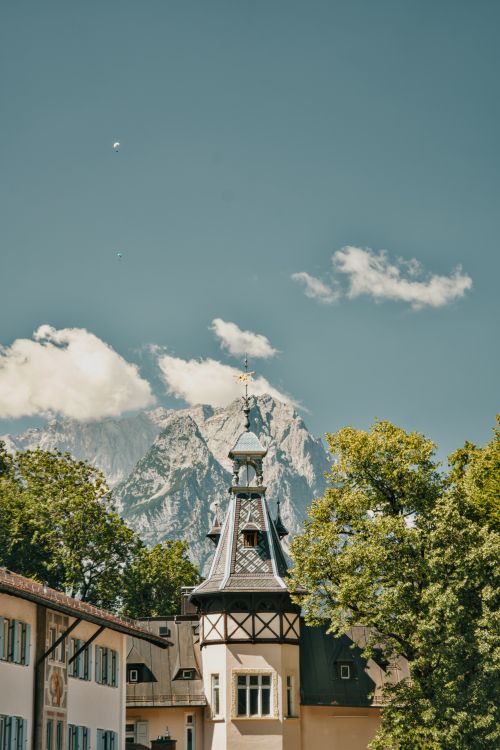 Free Charming German chapel tower framed by trees and majestic mountains under a clear sky. Stock Photo