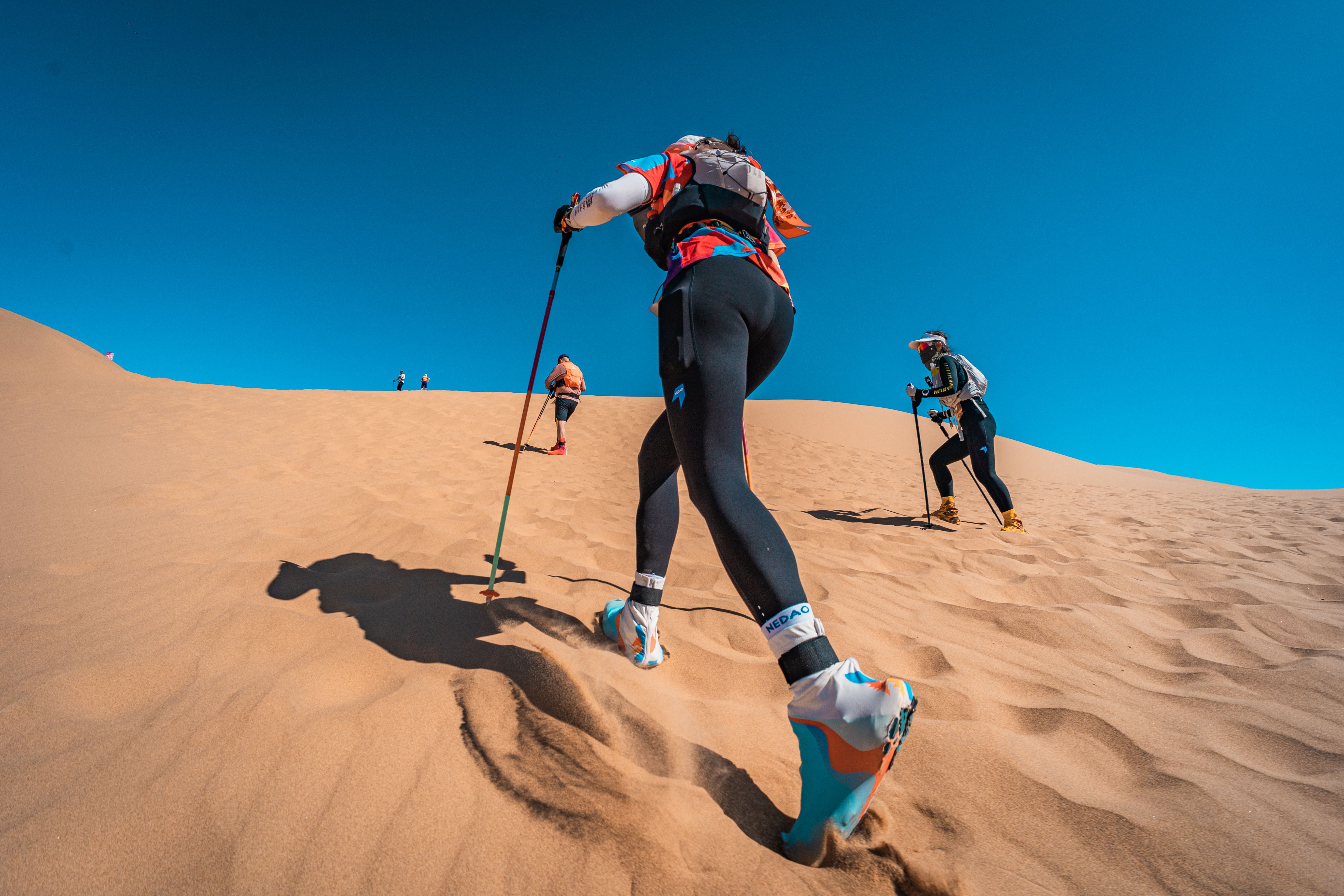 Athletes climb a sand dune during a desert marathon, showcasing endurance.