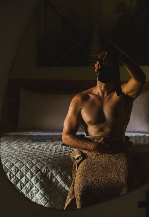 Free Dimly lit room with a muscular man relaxed in contemplation and mirror reflection. Stock Photo