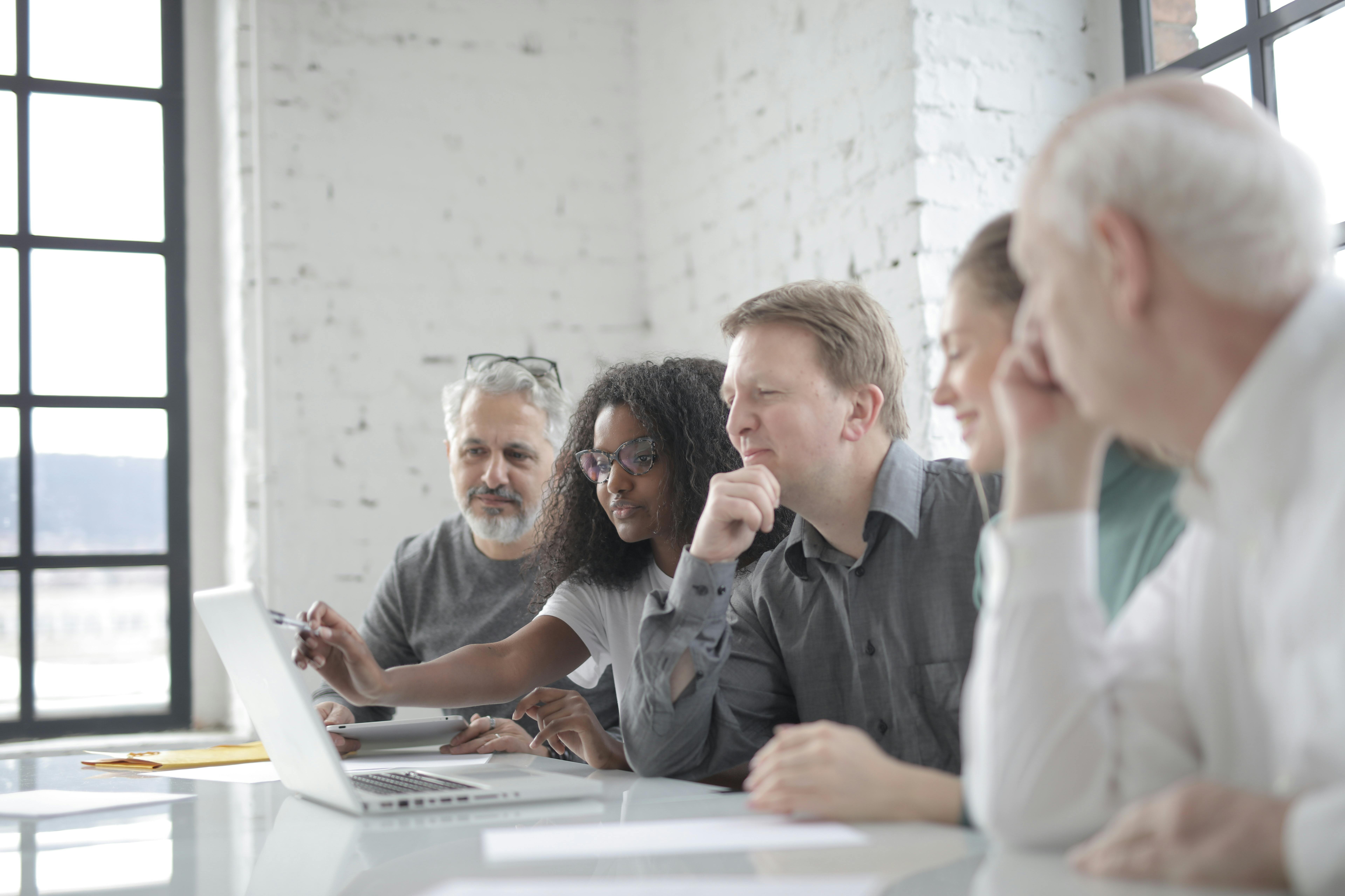 group of diverse colleagues discussing project while using laptop