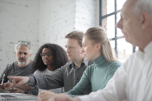 Serious male worker pointing with finger at netbook screen during meeting while sitting with diverse partners in office in afternoon