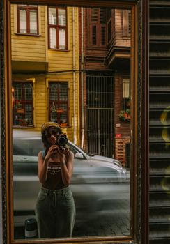 Woman taking a mirror selfie in a vibrant Istanbul street, capturing lively urban reflections.