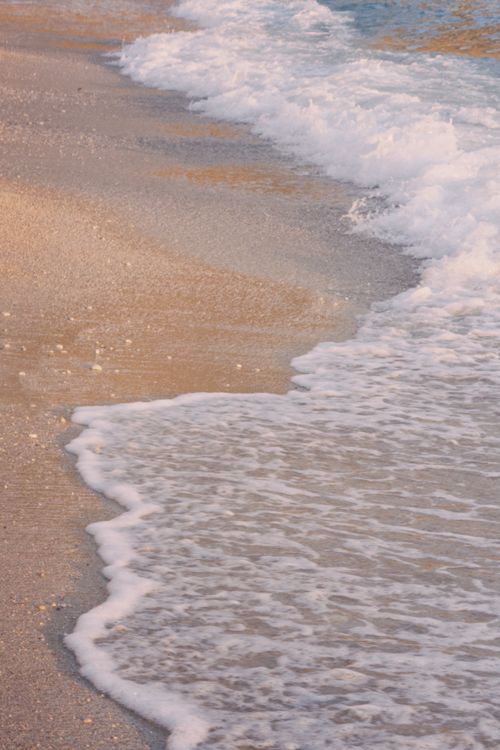 Free Gentle waves washing up on a sandy beach during sunset, creating a peaceful and warm ambiance. Stock Photo