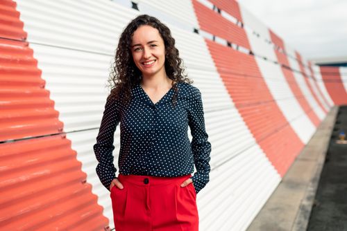 Free Chic portrait of a smiling woman in patterned blouse and red pants with a dynamic striped backdrop. Stock Photo