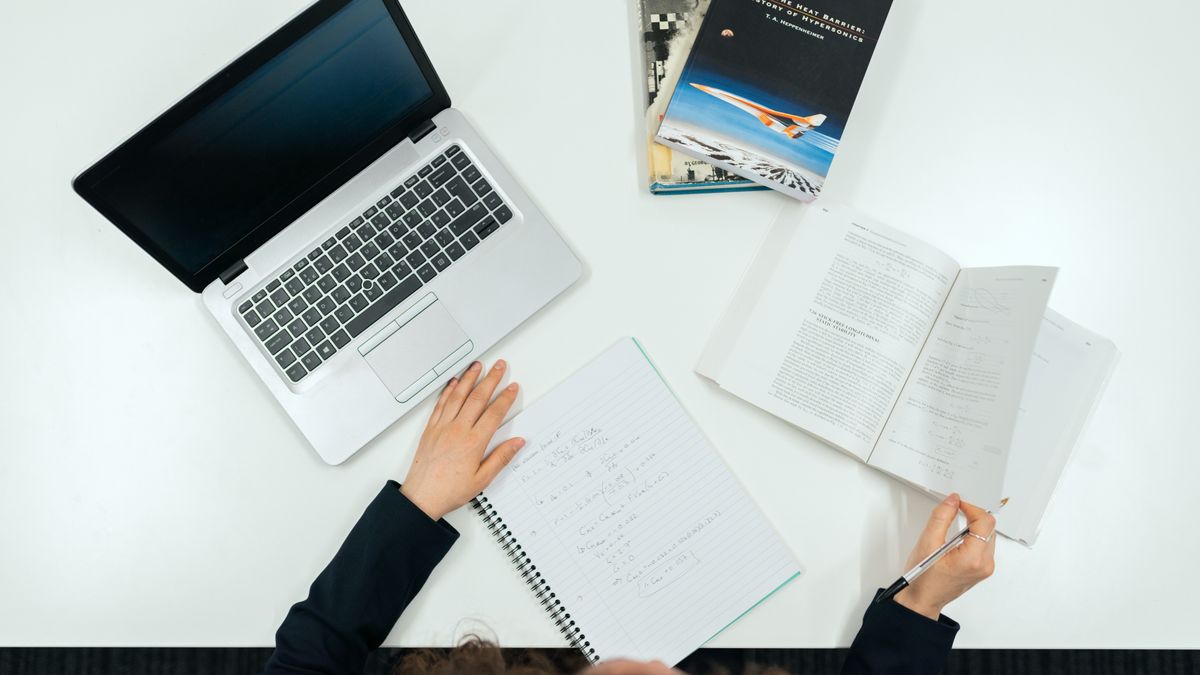 Top view of a work desk with laptop, books, and notes showcasing productivity.