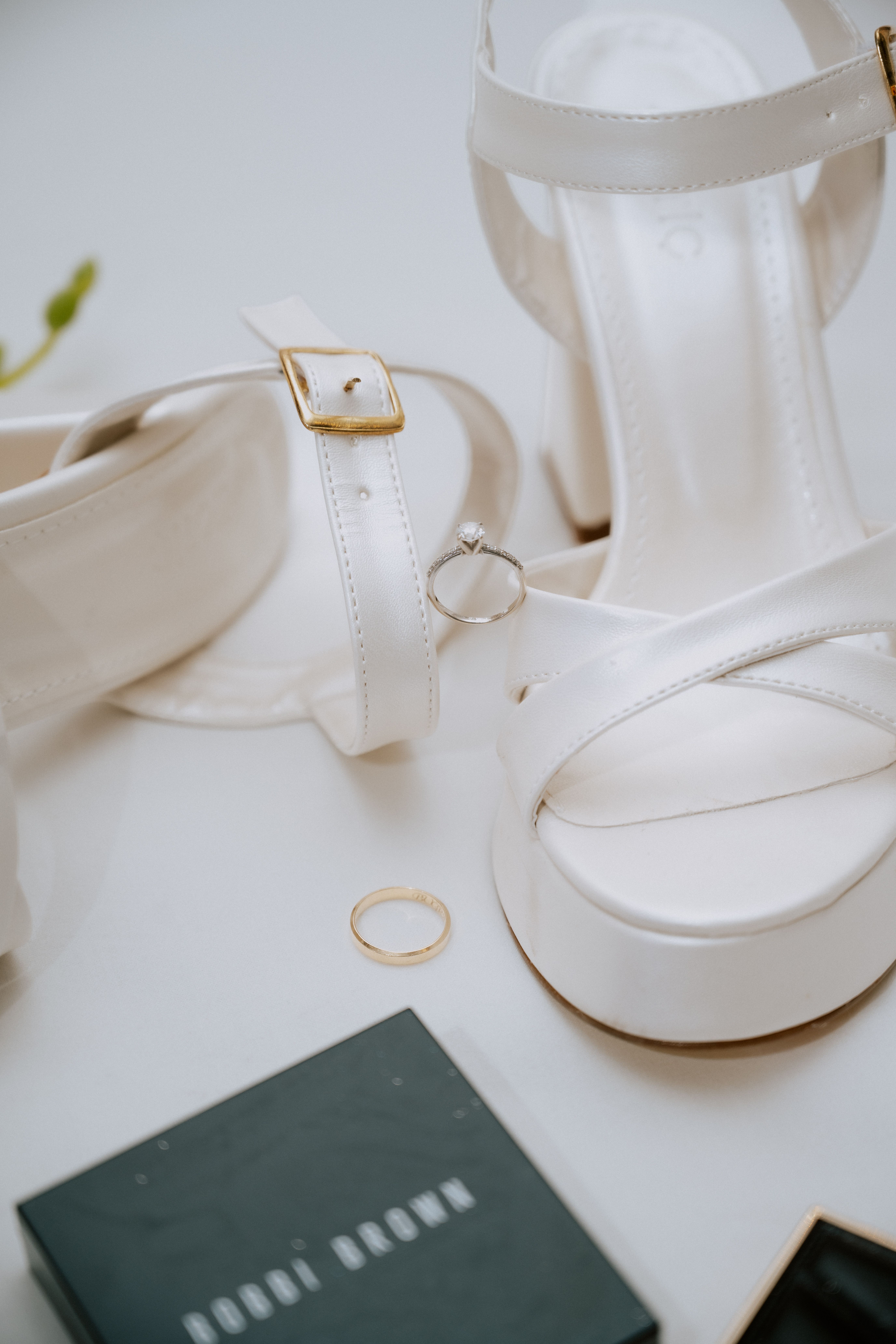 Close-up of elegant white bridal heels, gold ring, and makeup, perfect for a wedding day.