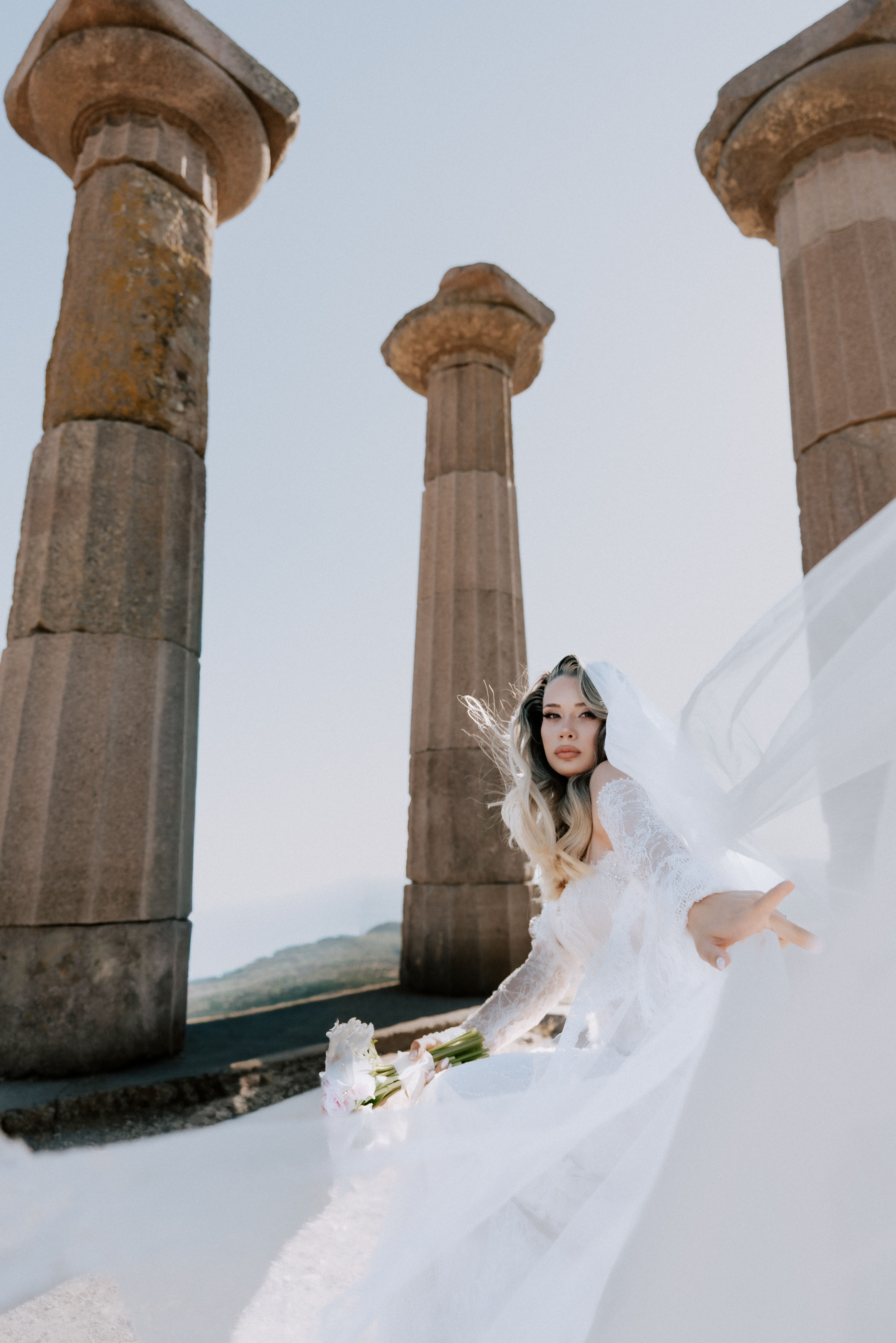 Bride in white gown among ancient temple columns in Çanakkale, Türkiye.