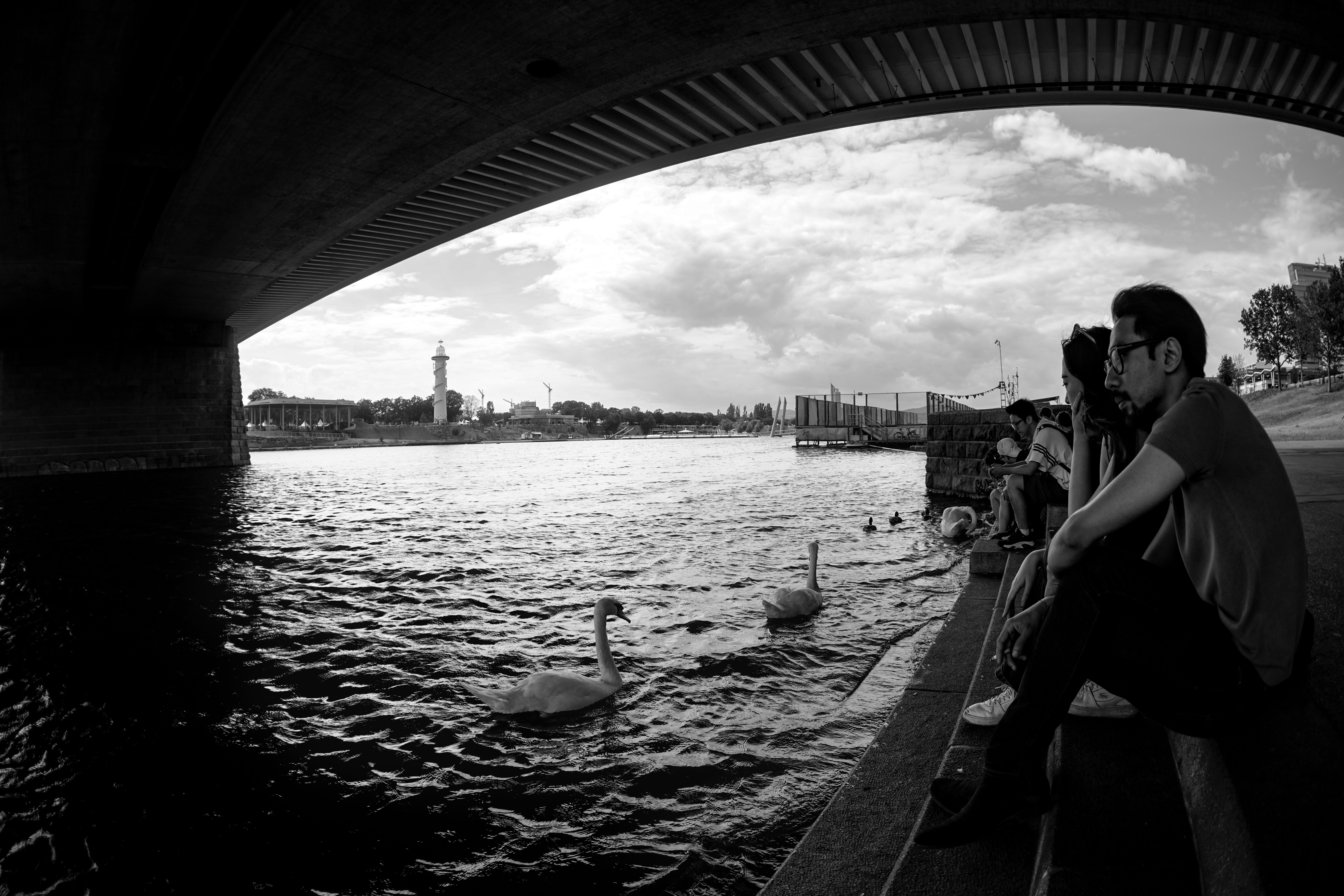 Monochrome view of people by the river under a bridge in Vienna, Austria.