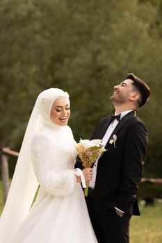 Bride in hijab and groom share a joyful moment outdoors on their wedding day.