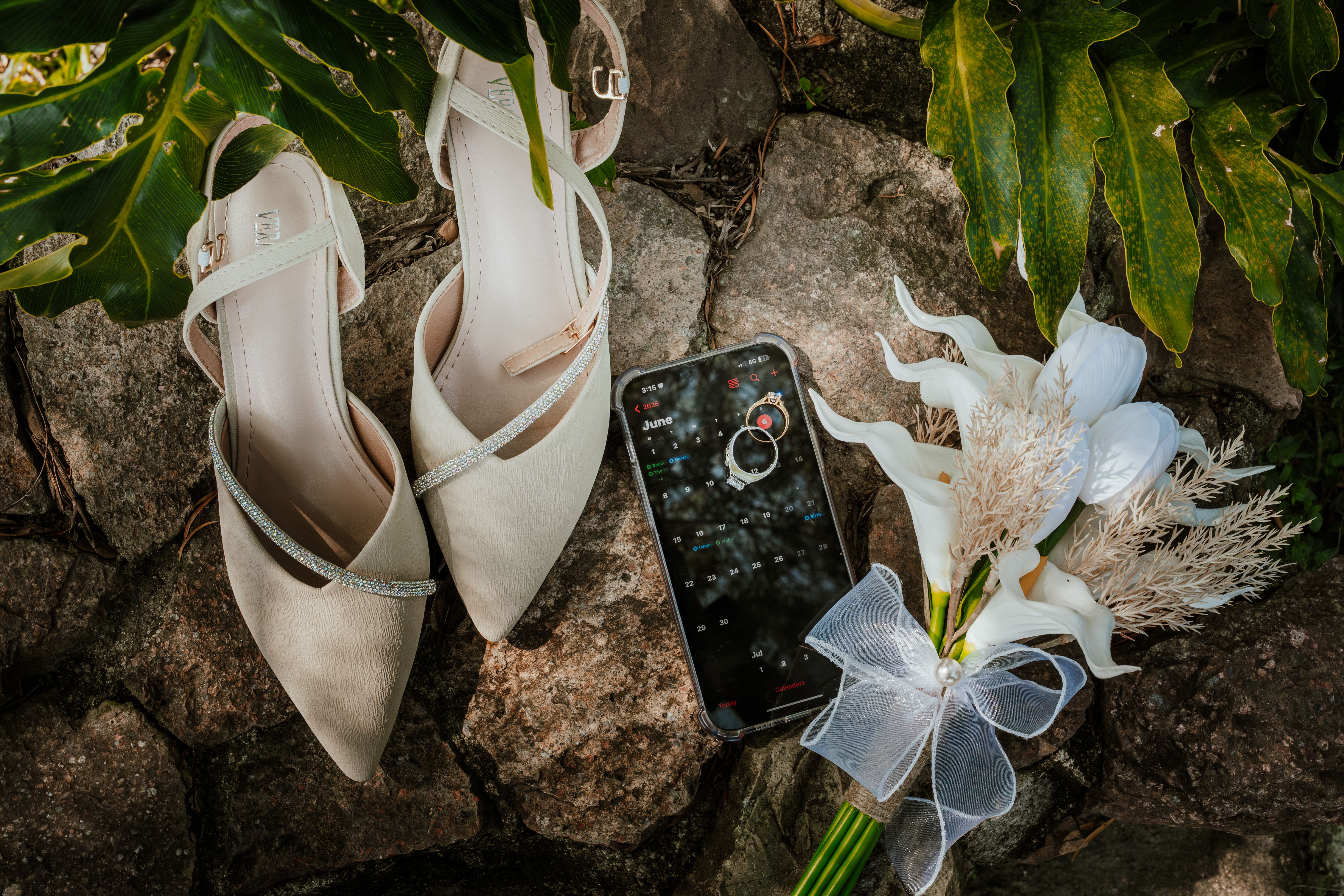 A flat lay of wedding accessories on rocks with shoes, phone, and bouquet
