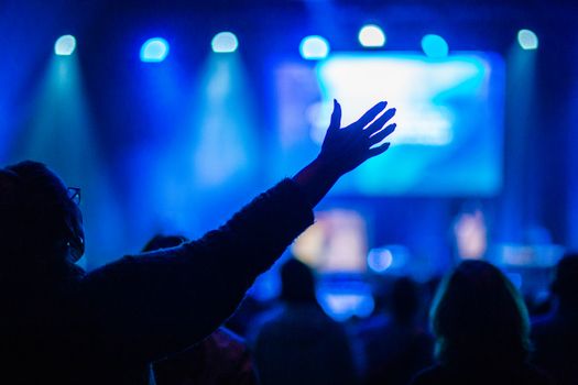 Back view of crop unrecognizable woman in eyeglasses with outstretched arms enjoying concert in dark club with neon spotlights