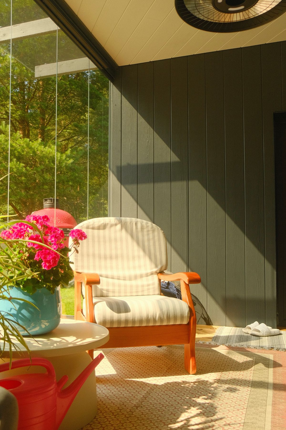 Bright sunlit porch with a cozy chair and vibrant flowers, perfect for relaxation. Stock Photo.
