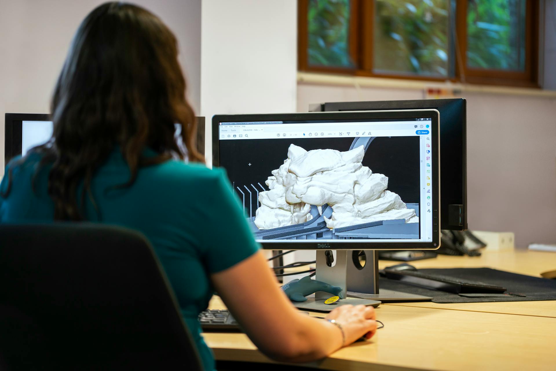 A woman using CAD software for 3D modeling in an office setting with a back view.