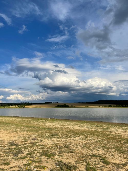 Free Serene lake under expansive sky with dynamic clouds and scenic landscape. Stock Photo