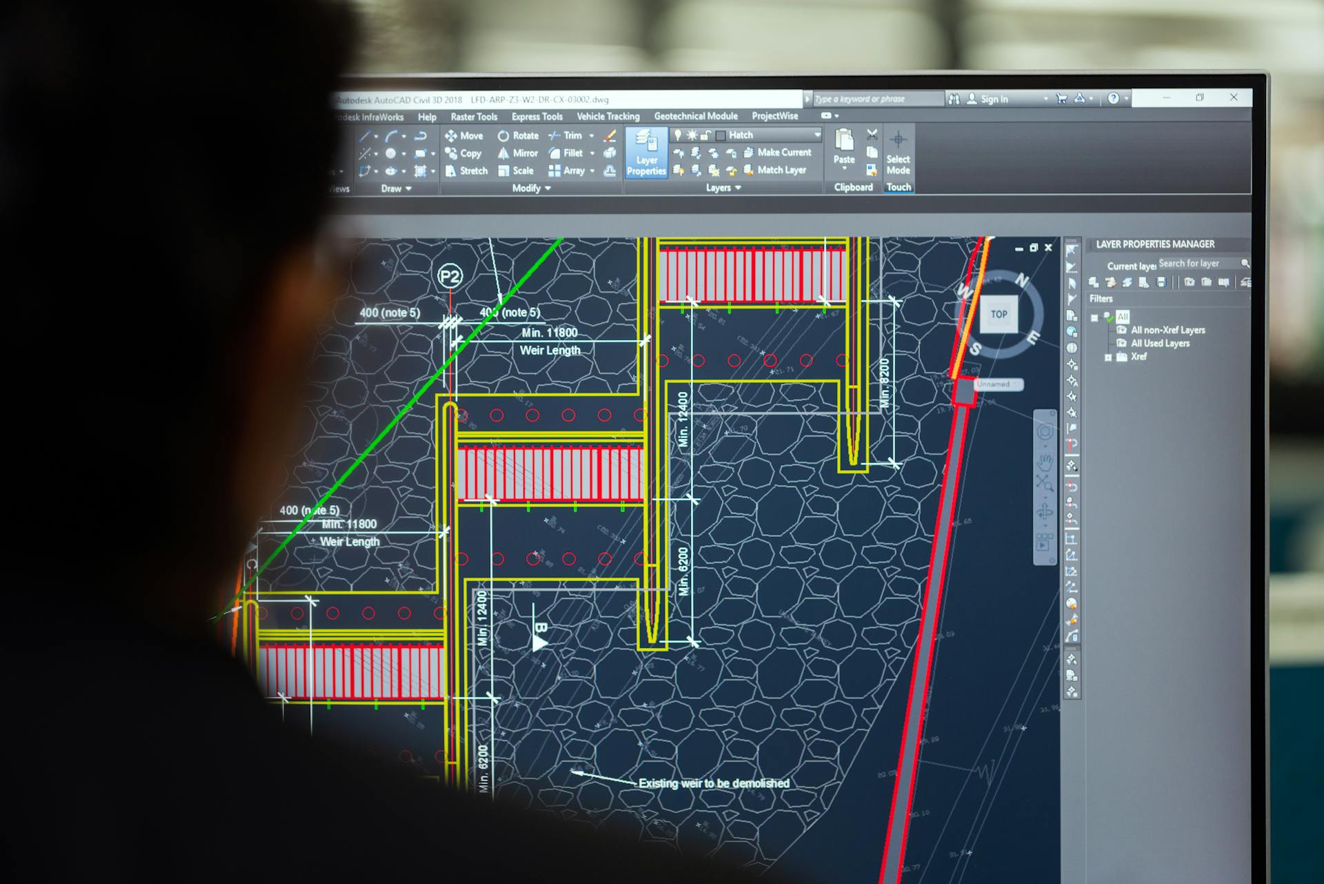 A civil engineer working on a weir design using CAD software on a computer screen in an office setting.