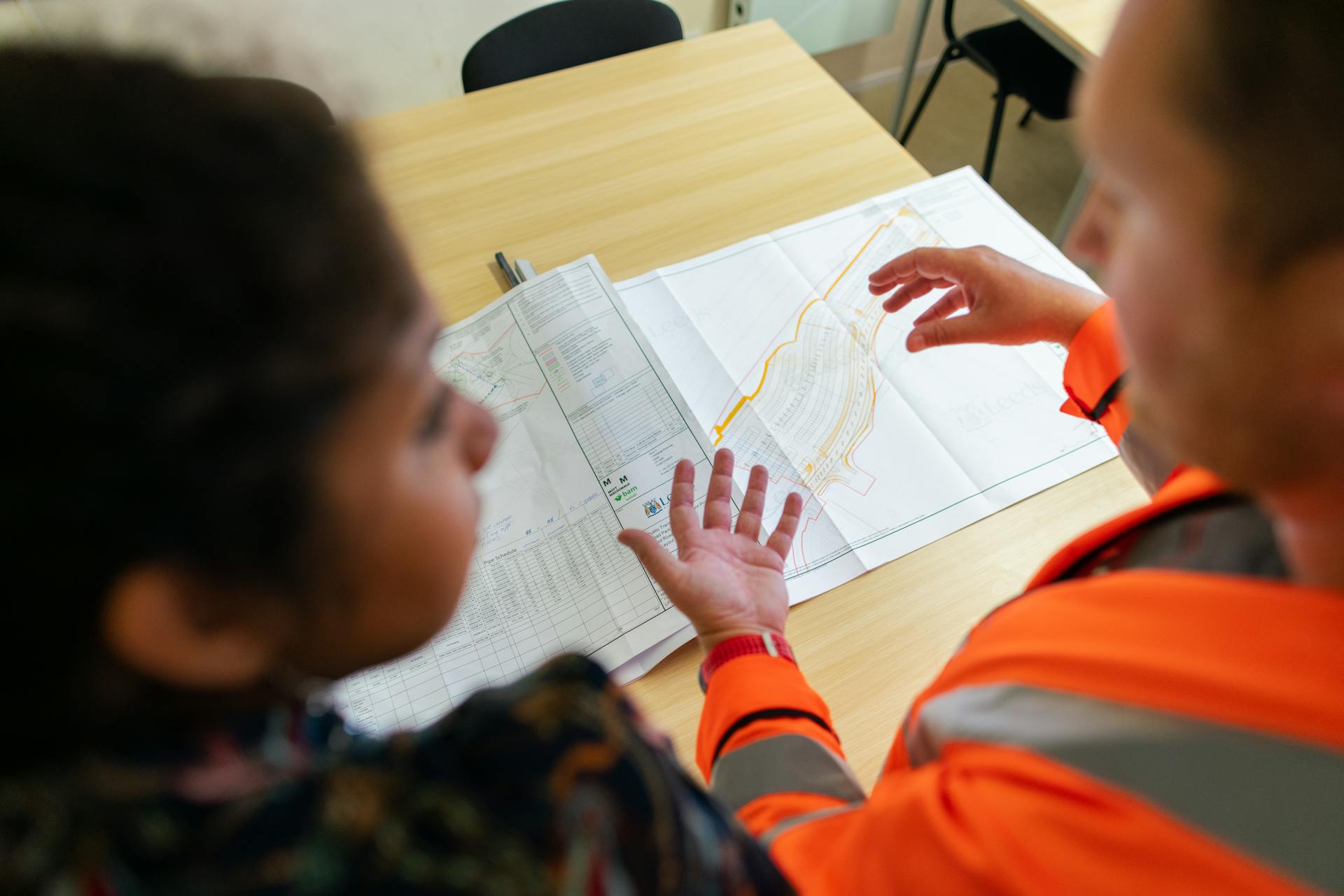 Two engineers reviewing construction blueprints on a table in an office setting.