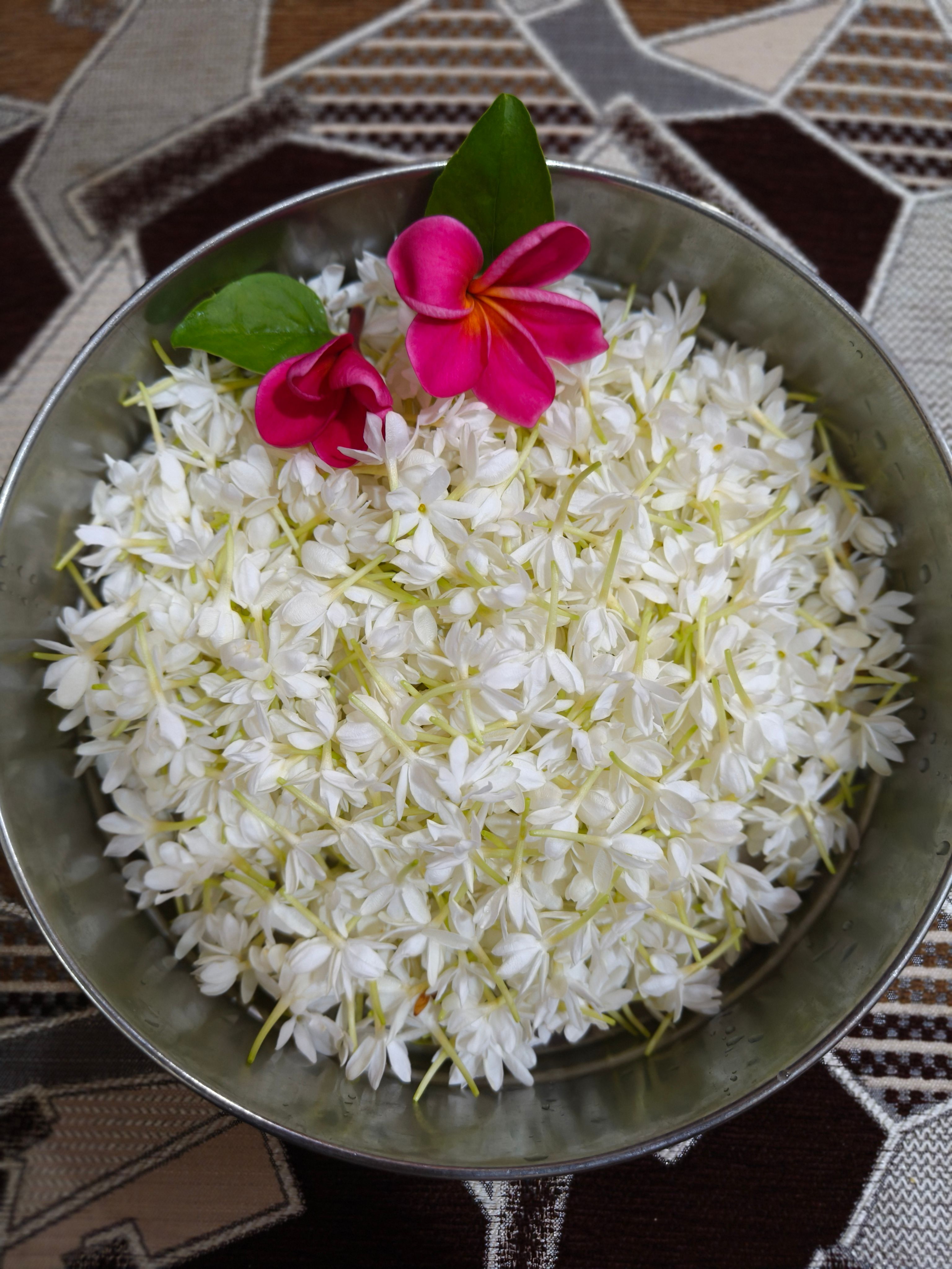A bowl filled with fresh jasmine flowers adorned with vibrant pink plumeria blooms, perfect for decor.
