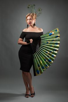Woman in black dress with peacock feather fan in a studio setting.