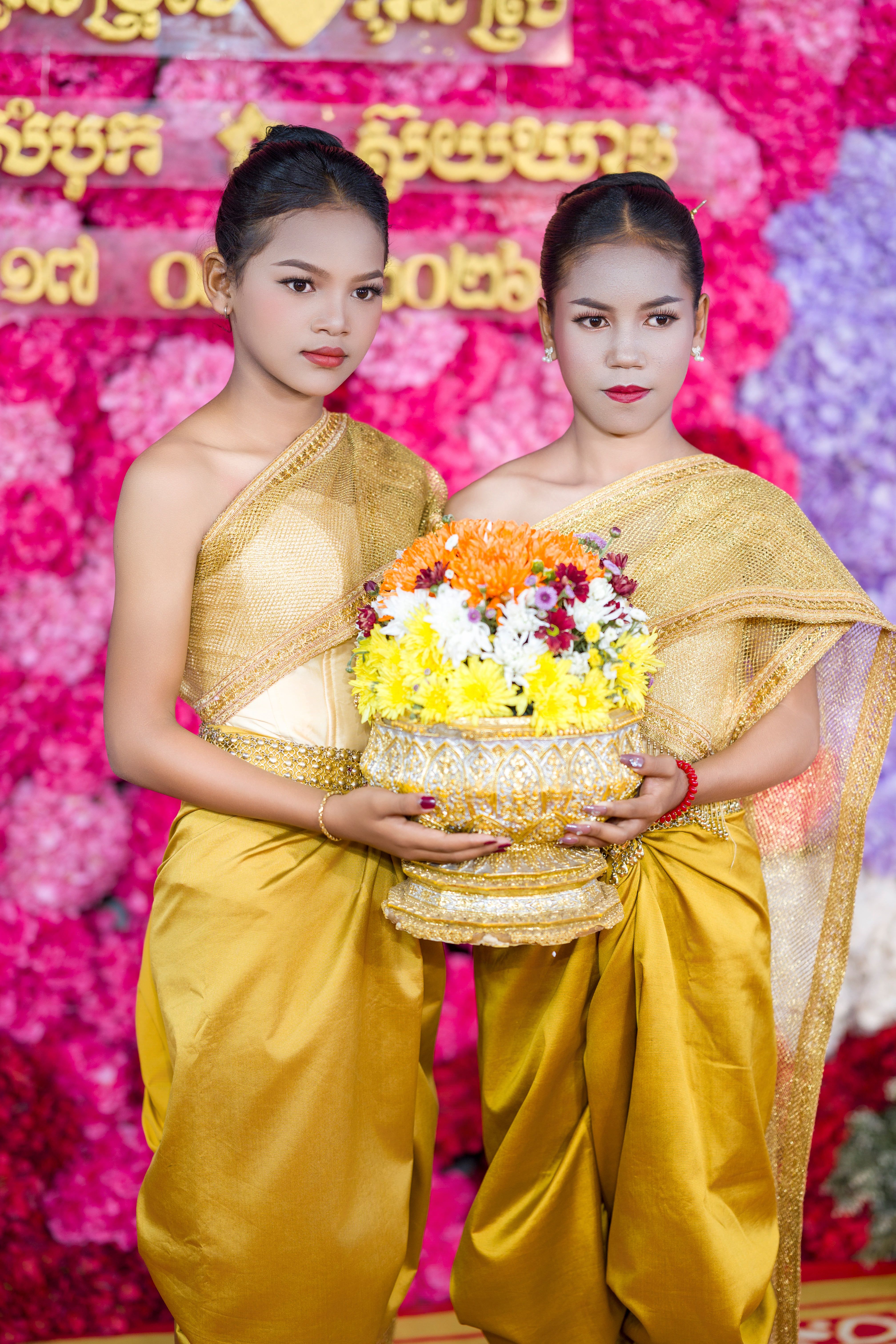 Two women in traditional Cambodian attire hold a flower garland, symbolizing cultural heritage and celebration.