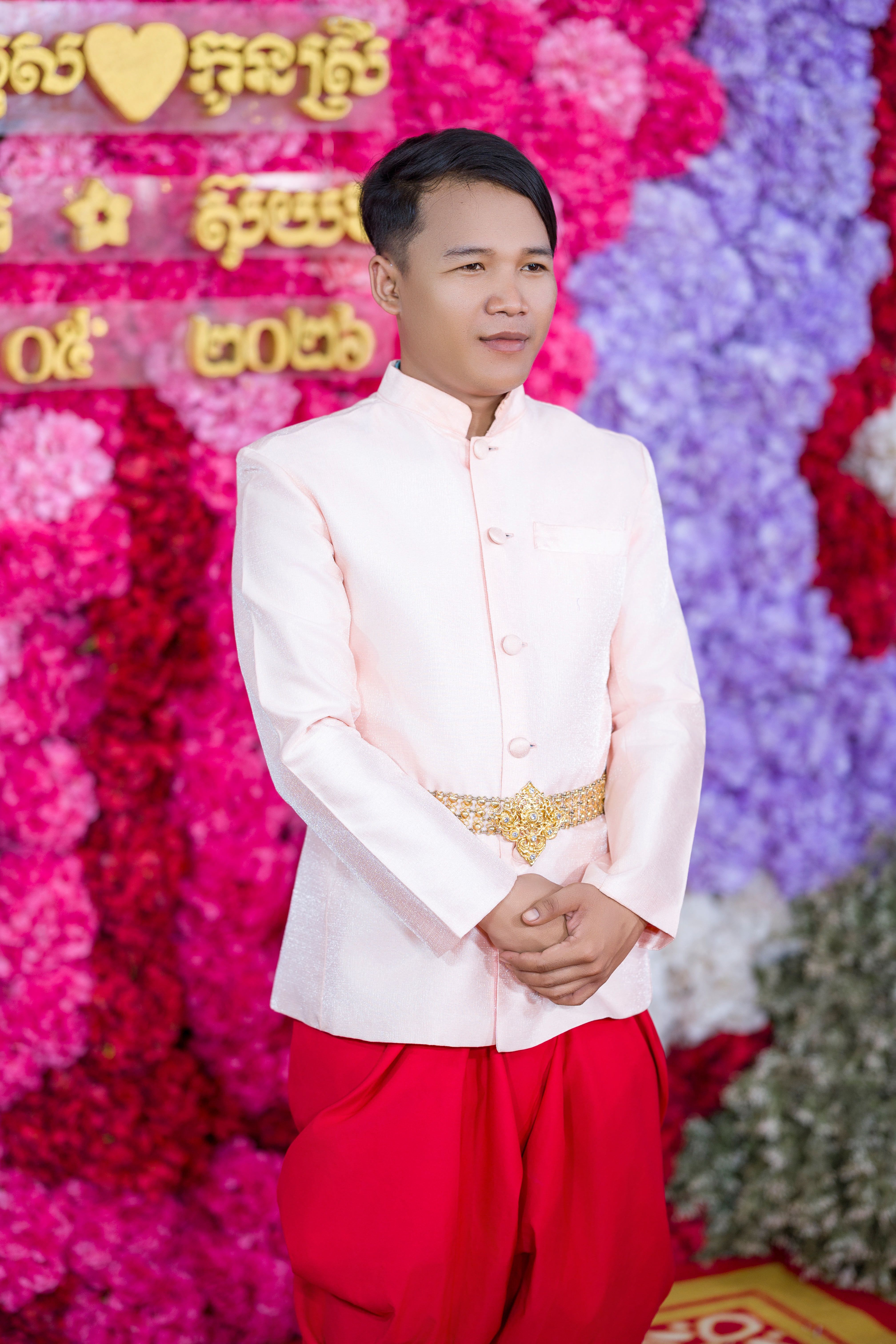 Man in traditional Cambodian wedding attire with colorful backdrop.