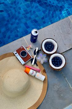 Flat lay of poolside essentials: camera, drinks, sunglasses, sunscreen, and fruits.
