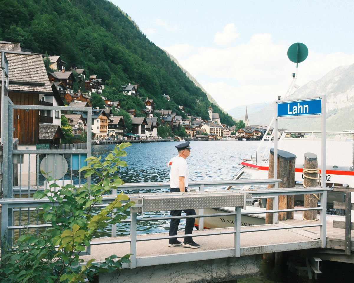 A picturesque scene of Hallstatt village viewed from Lahn dock, featuring a ferry and lush green mountains.