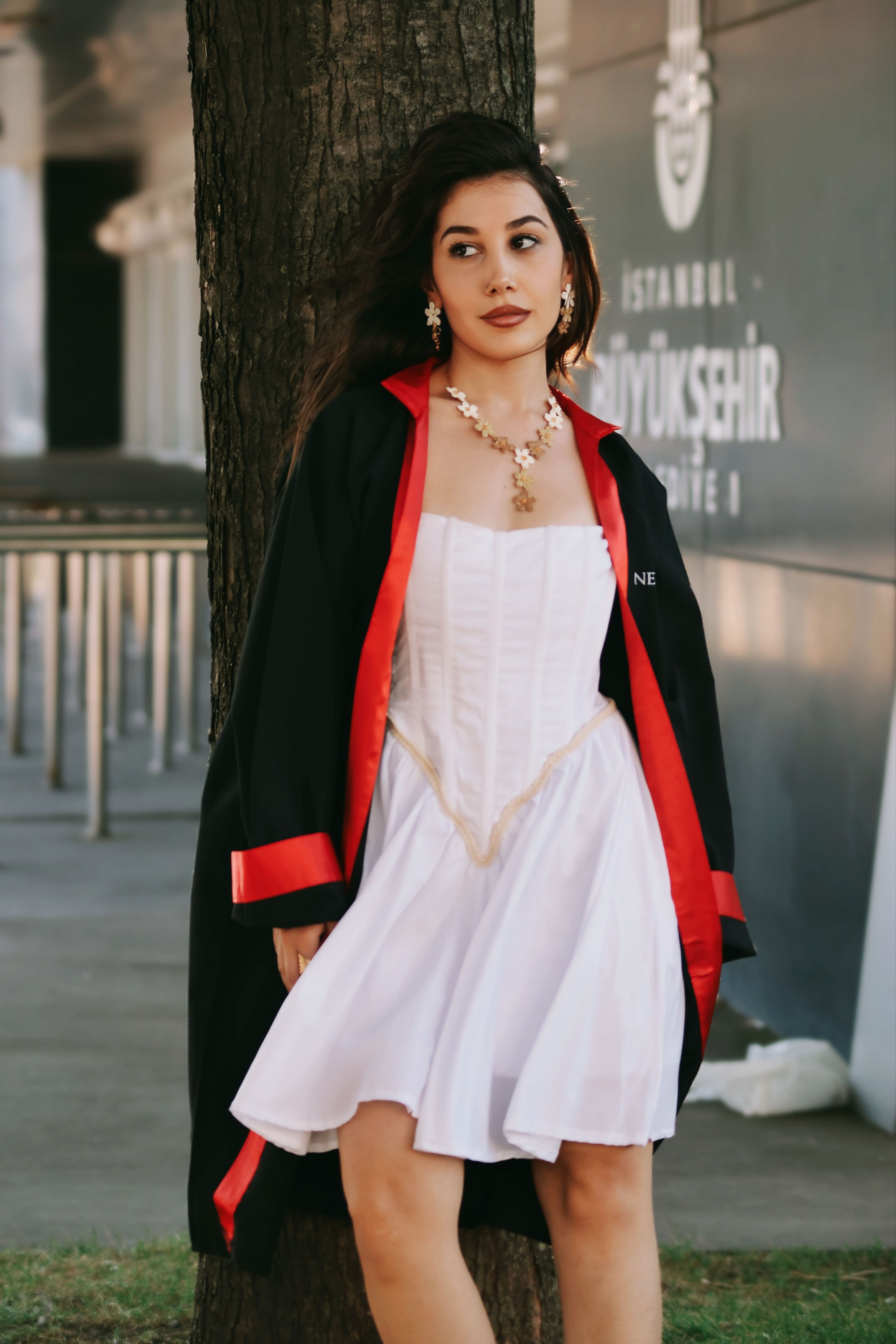 Stylish woman in a white dress under graduation gown outdoors.