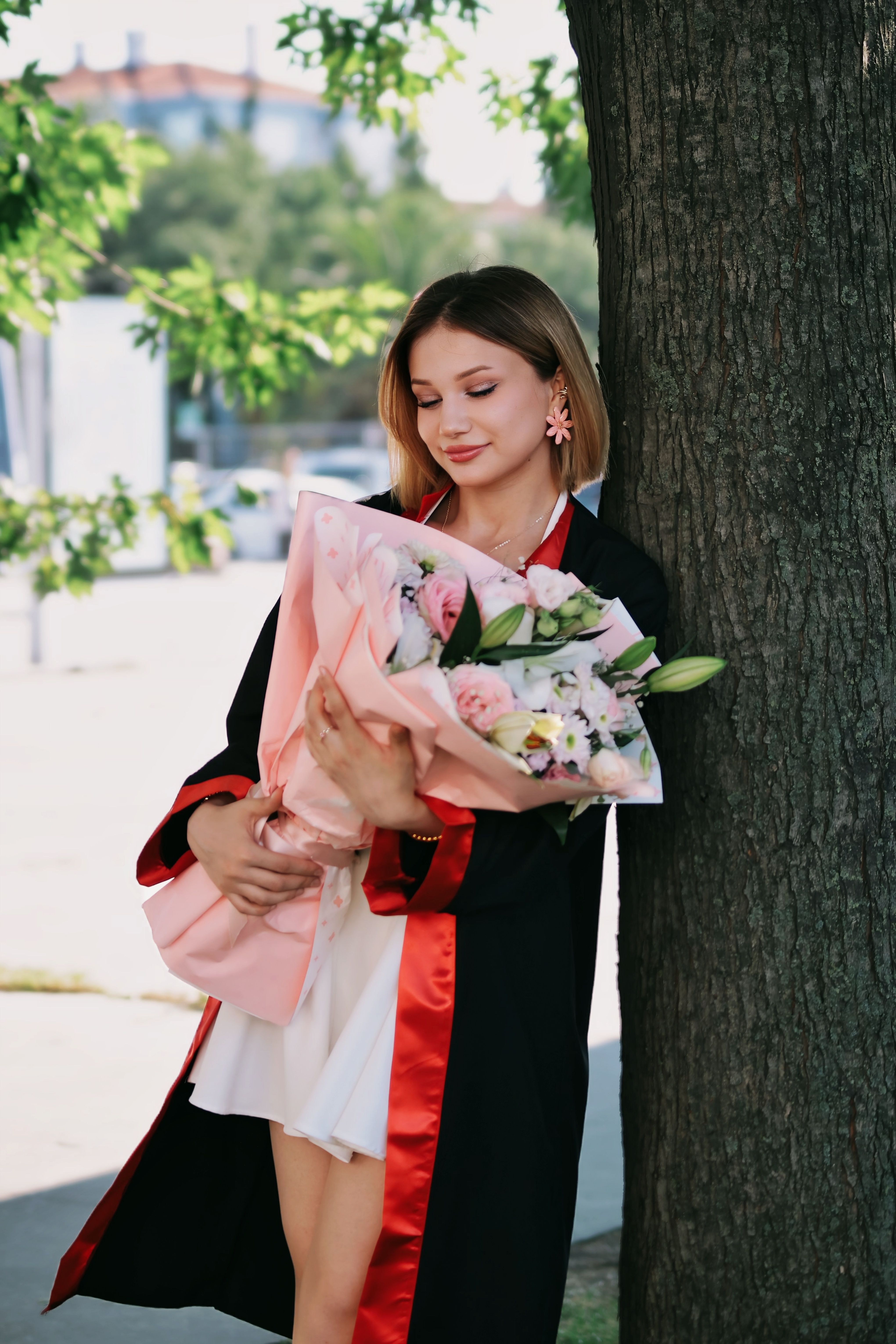 [ColoSach]-young-graduate-holding-a-floral-bouquet,-standing-by-a-tree-on-a-sunny-afternoon.