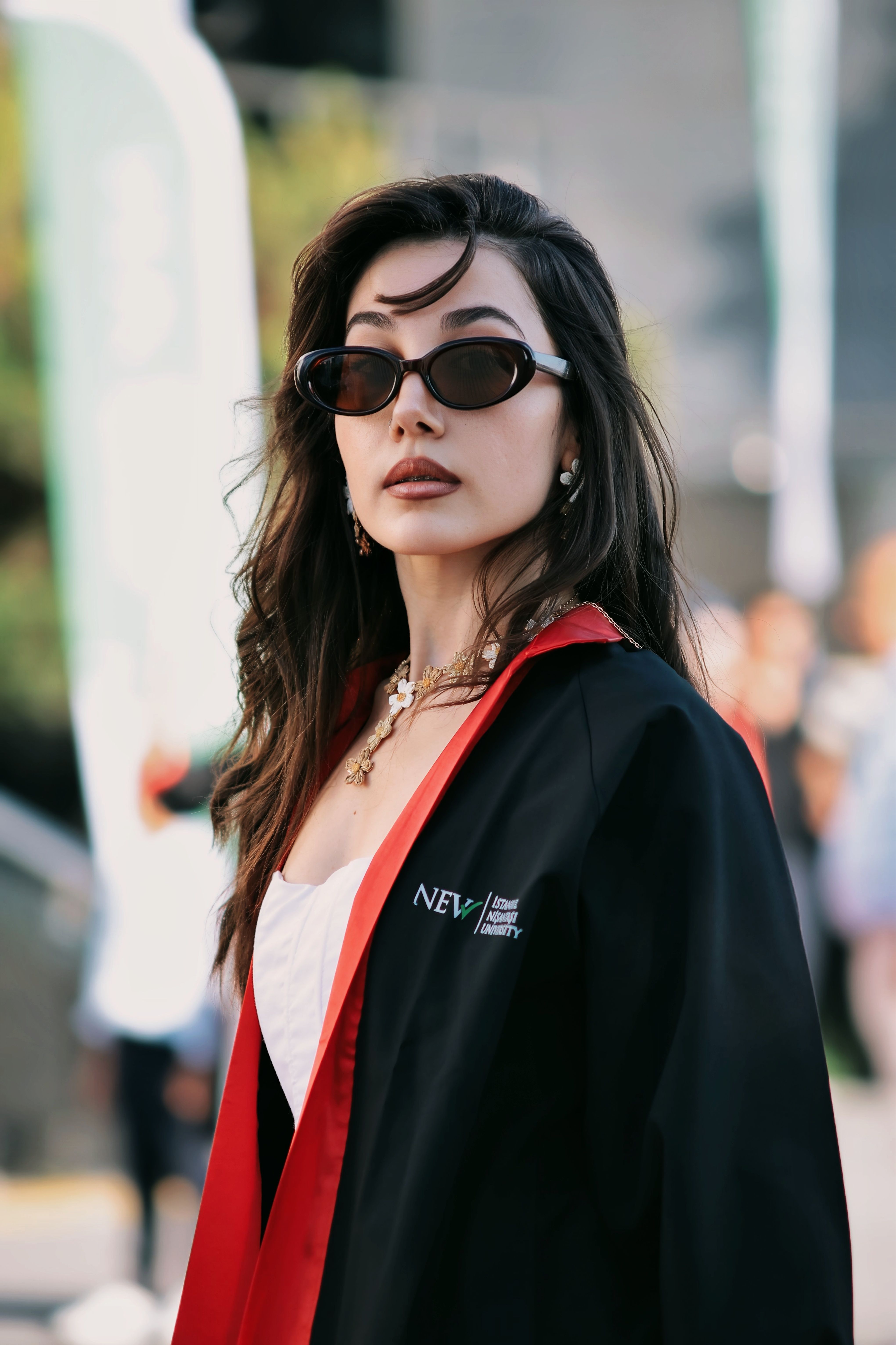 Elegant woman in graduation attire and sunglasses outdoors, embodying fashion and achievement.