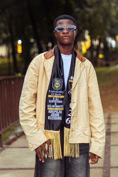 A proud graduate poses outdoors in a fashionable outfit, showcasing their achievement.