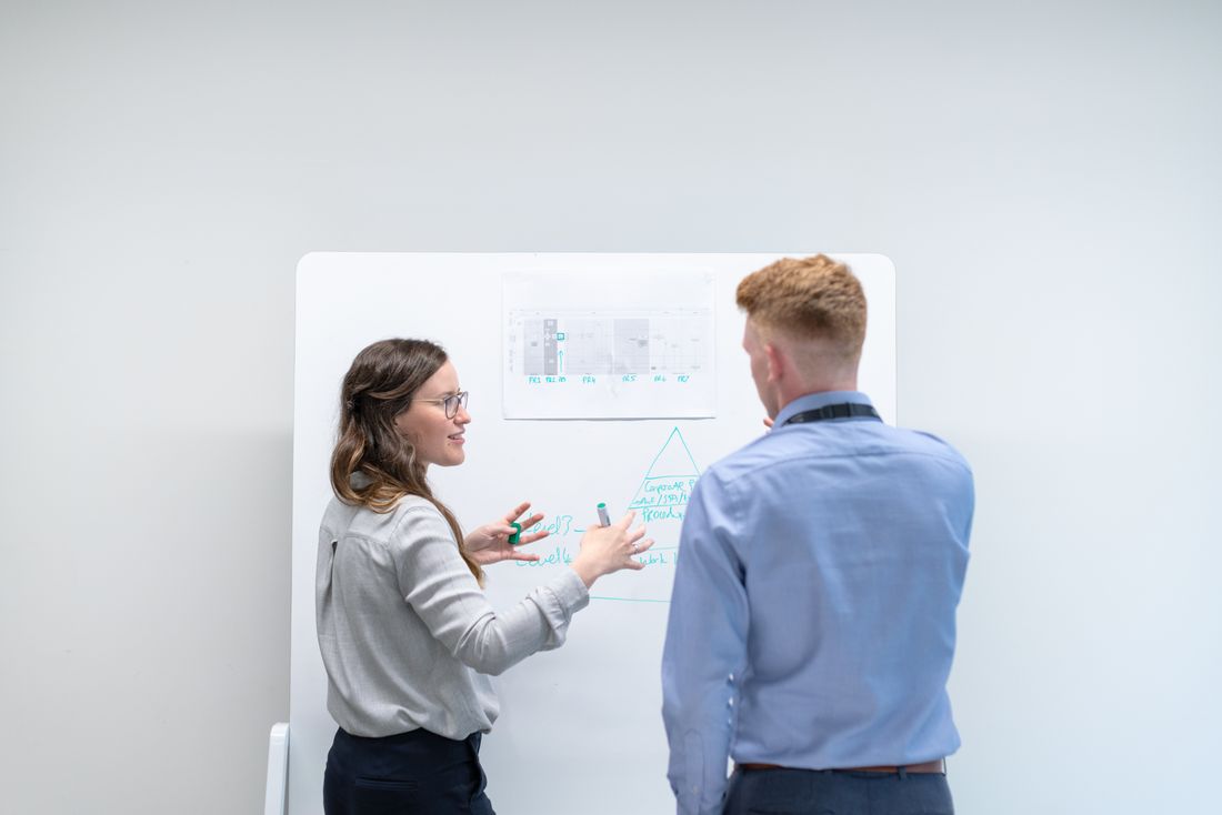 Two professionals discussing project plans at whiteboard in office setting