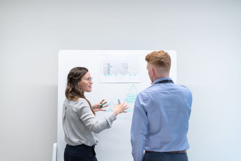 Zwei Beratende diskutieren eine Skizze an einem Whiteboard in einem hellen Büro