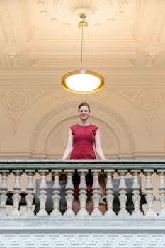 一名身穿红色连衣裙的女子站在室内经典建筑的阳台上