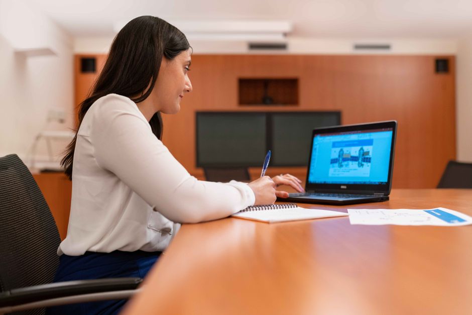 Mulher profissional trabalhando em um laptop em um ambiente de escritório moderno.