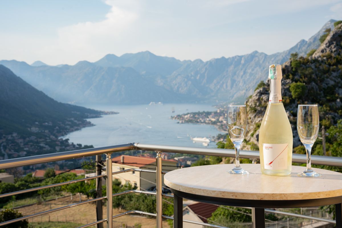 Două pahare și o sticlă pe balustrada unei terase, cu Golful Kotor în fundal