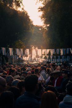 Crowds gather at a vibrant street festival in Buenos Aires, adorned with flags and morning sunlight.