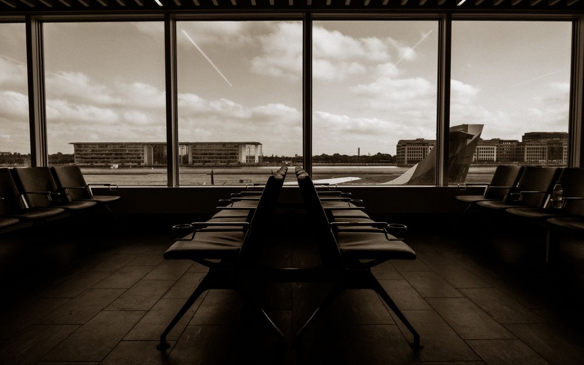 Quiet airport terminal in sepia tone overlooking runway and airplane wing.
