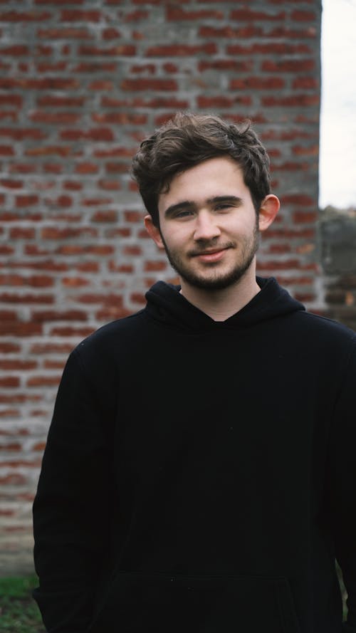 Smiling young man standing on street near brick wall