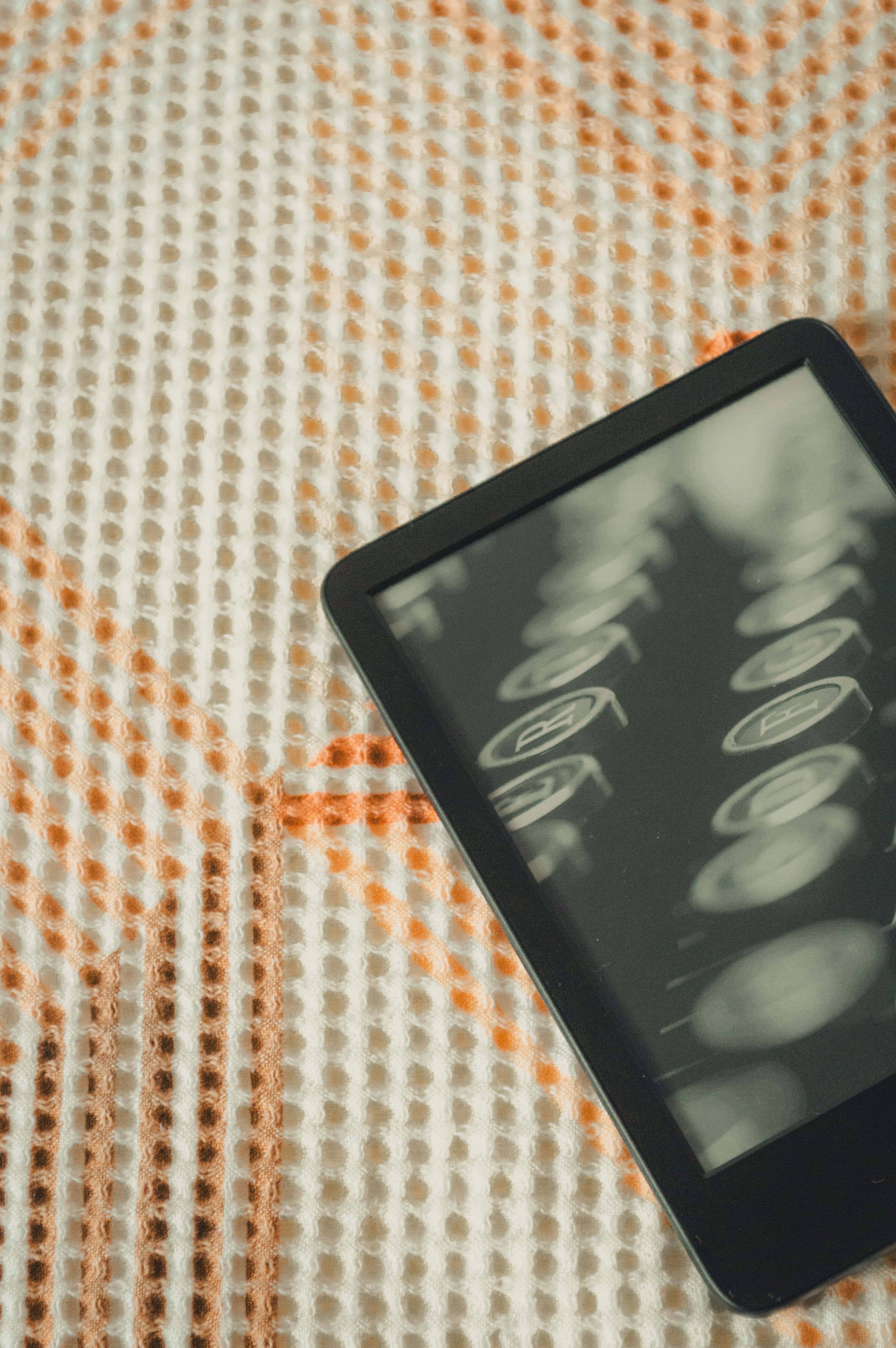 A sleek e-reader device resting on a textured fabric surface with a vintage effect.