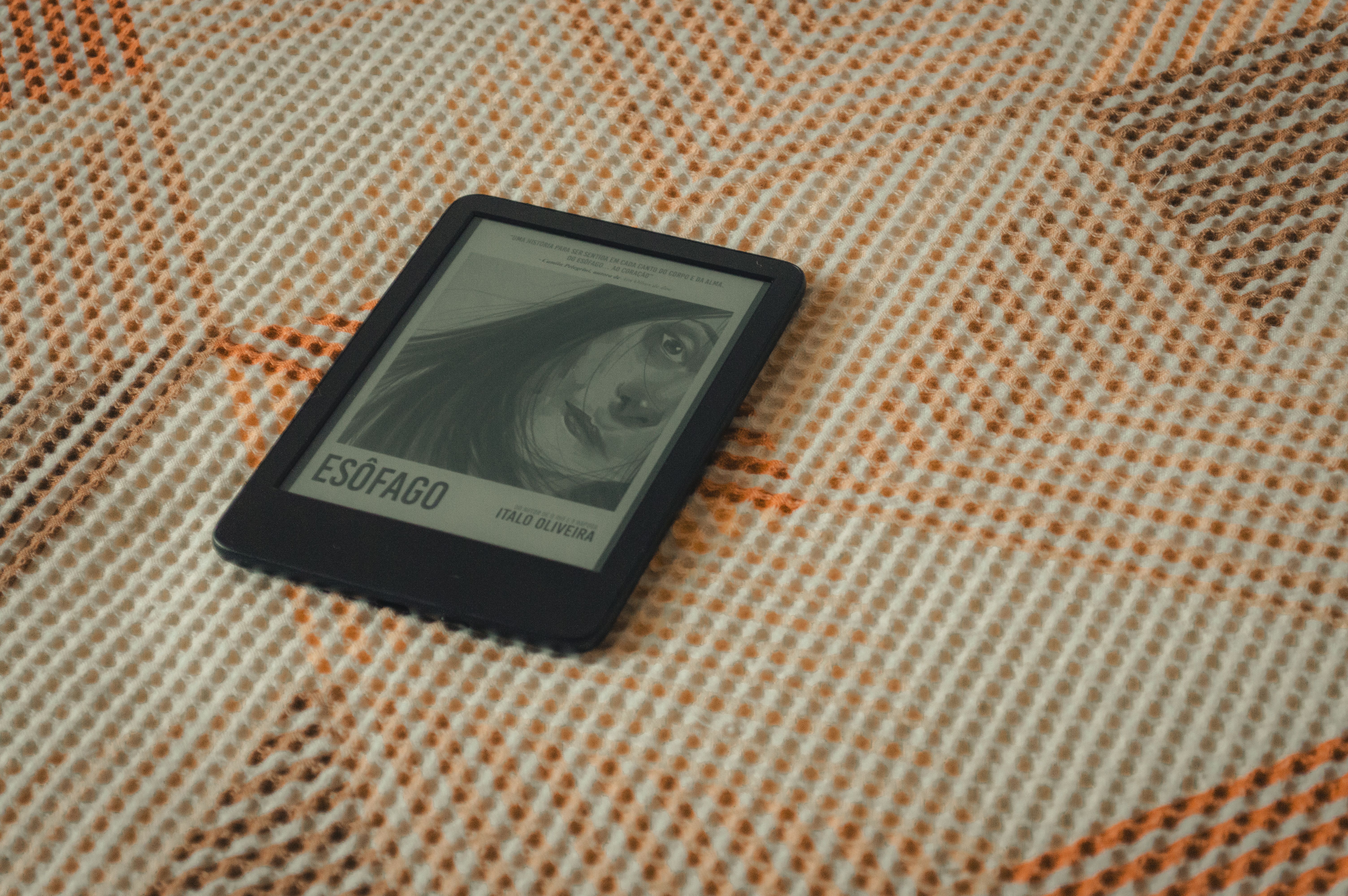 An e-reader displaying a book cover placed on a patterned fabric with warm tones.
