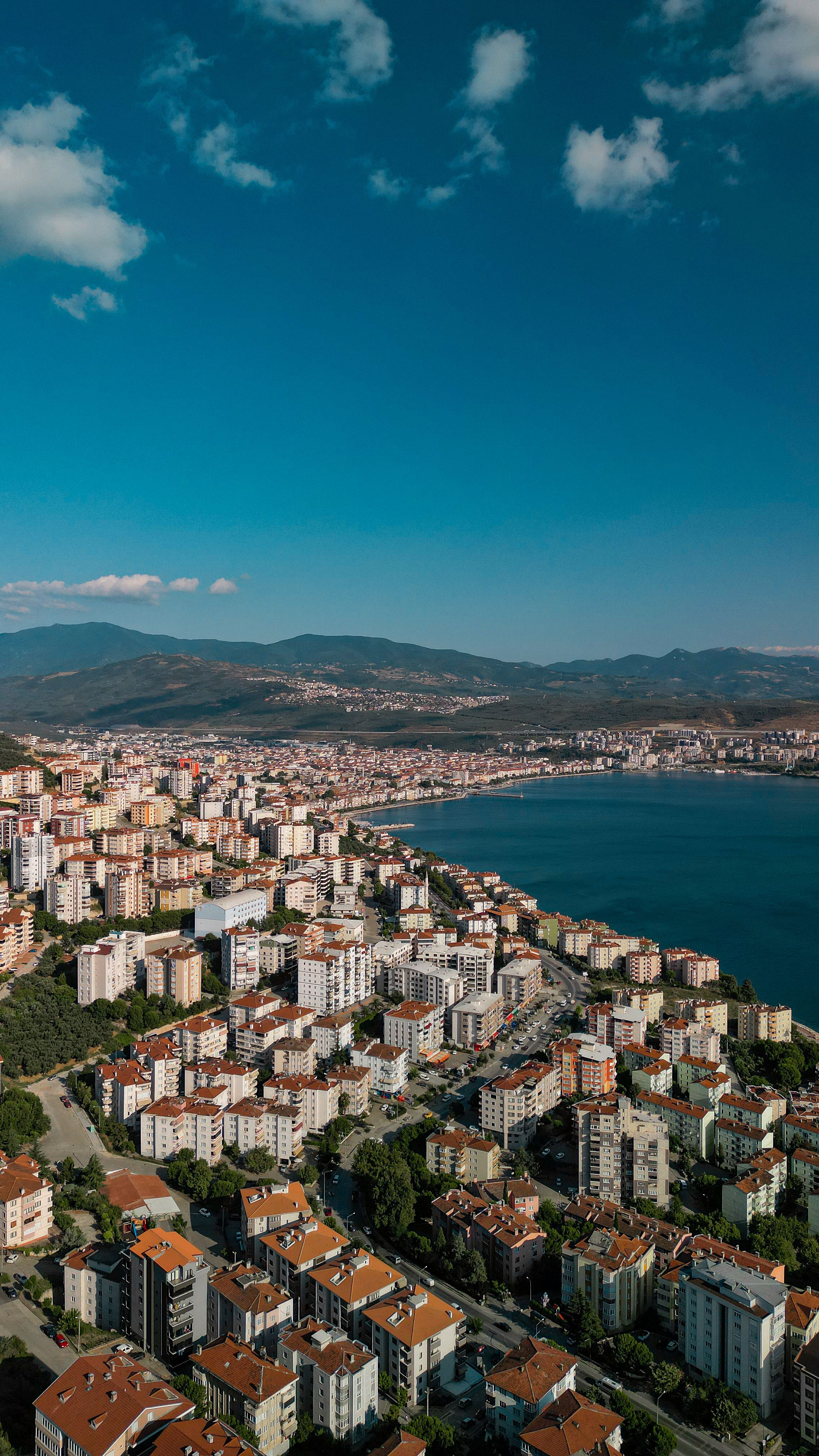 A breathtaking aerial shot capturing a coastal city with mountains and the sea under a clear sky.