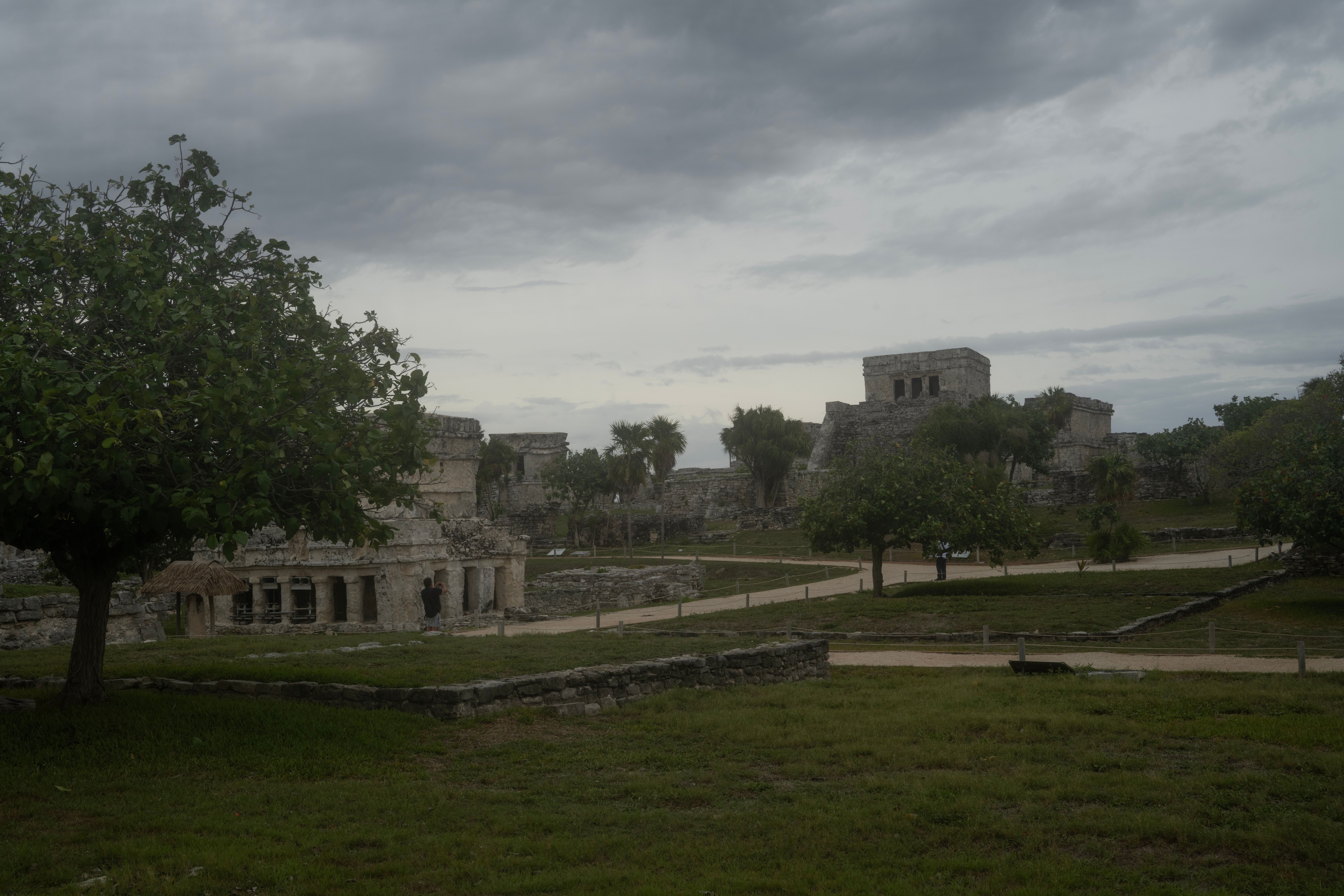 Explore the historic ruins of Tulum in Mexico surrounded by lush trees and overcast skies.