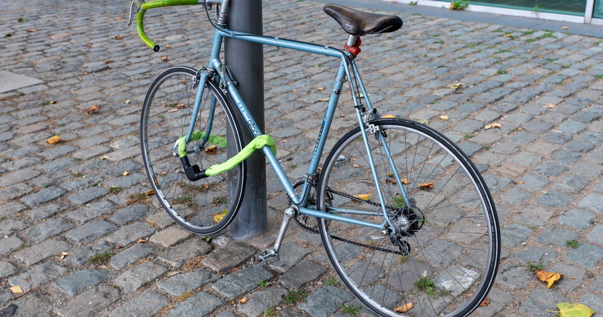 A road bike locked to a lamppost with a green cable lock