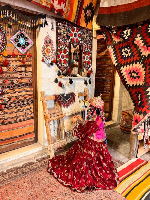 Free A woman weaving on a loom surrounded by colorful textiles in a traditional shop. Stock Photo